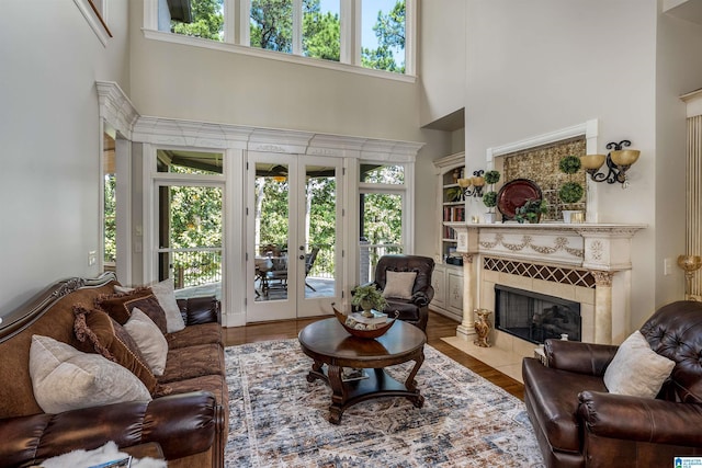 living room with a tiled fireplace, a towering ceiling, light hardwood / wood-style floors, and french doors