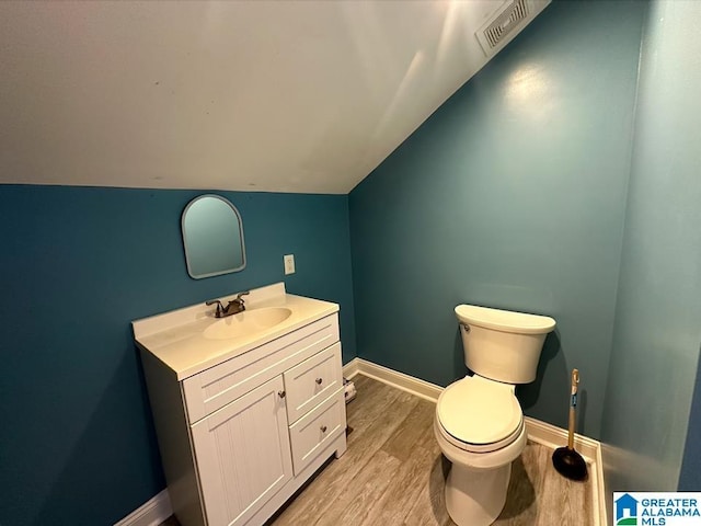 bathroom with hardwood / wood-style flooring, vaulted ceiling, vanity, and toilet