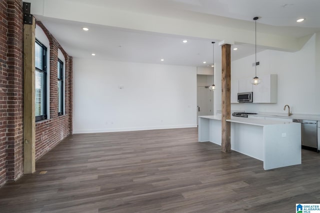 kitchen featuring dark hardwood / wood-style floors, sink, hanging light fixtures, stainless steel appliances, and brick wall