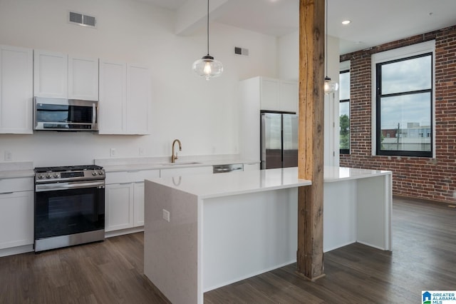 kitchen with pendant lighting, sink, white cabinetry, appliances with stainless steel finishes, and brick wall