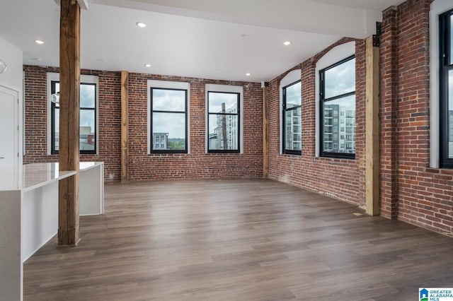 unfurnished living room with beamed ceiling, brick wall, and hardwood / wood-style floors