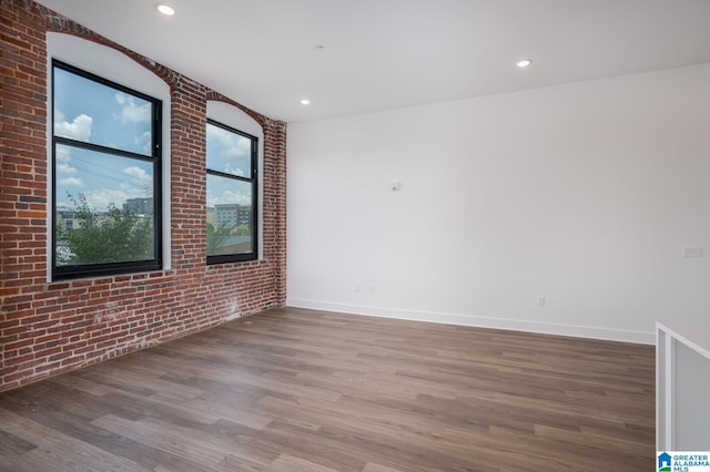 unfurnished room featuring brick wall and hardwood / wood-style flooring