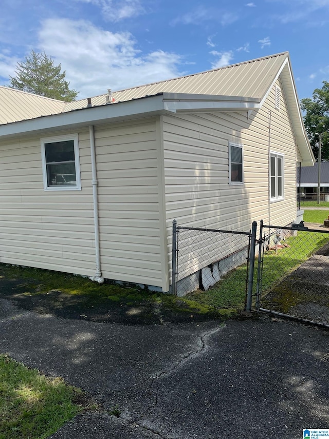 view of side of home with fence, metal roof, and a gate