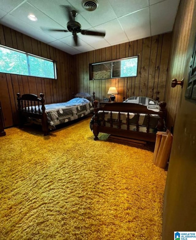 bedroom featuring a paneled ceiling, carpet, wooden walls, and ceiling fan