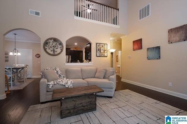 living room featuring ornamental molding, a notable chandelier, a towering ceiling, and hardwood / wood-style flooring