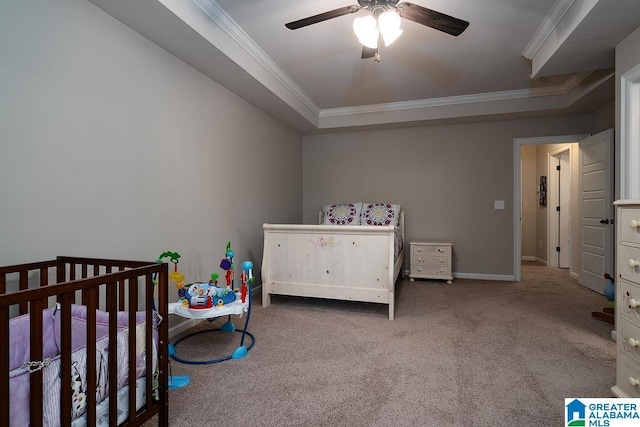 carpeted bedroom with a nursery area, ceiling fan, a tray ceiling, and crown molding