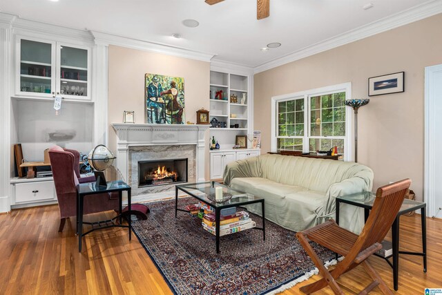 living room featuring built in shelves, a high end fireplace, crown molding, and hardwood / wood-style flooring