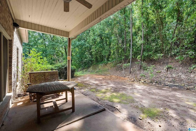 view of patio featuring a forest view, ceiling fan, and outdoor dining space