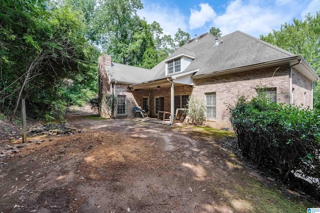 rear view of house featuring a shingled roof, a patio area, and brick siding