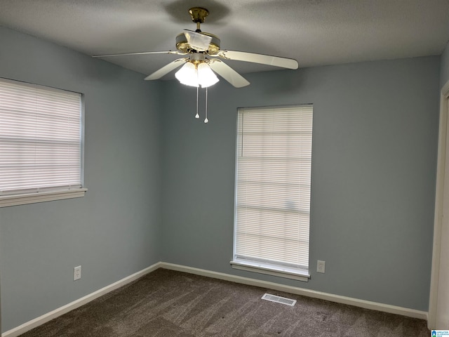 empty room featuring a healthy amount of sunlight, dark colored carpet, and ceiling fan