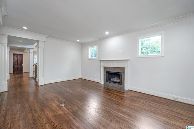 unfurnished living room featuring crown molding, a fireplace with flush hearth, decorative columns, and plenty of natural light