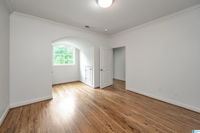 spare room featuring arched walkways, ornamental molding, baseboards, and wood finished floors