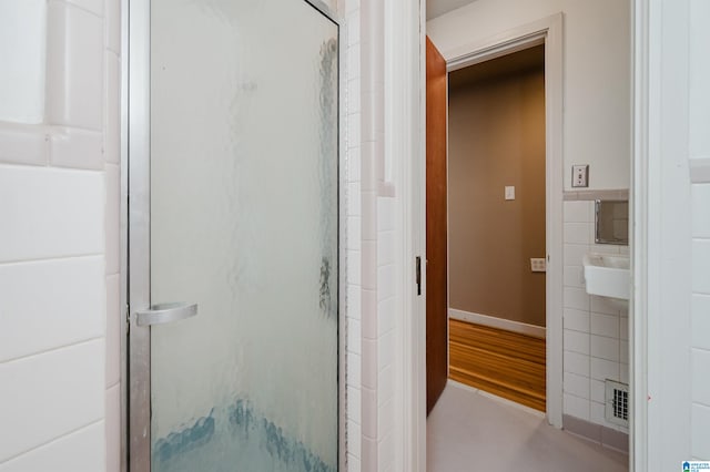 bathroom with a shower with shower door, hardwood / wood-style floors, and tile walls