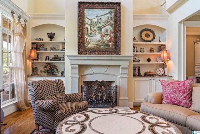 living room with built in shelves, hardwood / wood-style flooring, and ornamental molding