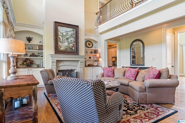 living room with built in shelves, light hardwood / wood-style floors, and a towering ceiling