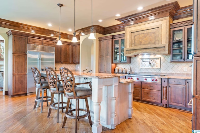 kitchen featuring decorative light fixtures, tasteful backsplash, light wood-type flooring, light stone counters, and appliances with stainless steel finishes