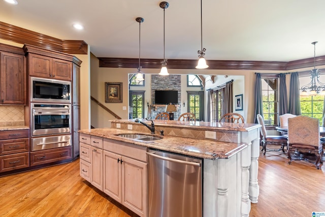 kitchen with stainless steel appliances, sink, light hardwood / wood-style floors, decorative backsplash, and a kitchen island with sink