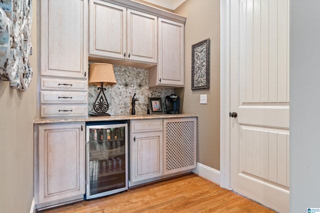 bar with light wood-type flooring, wine cooler, backsplash, light stone countertops, and ornamental molding