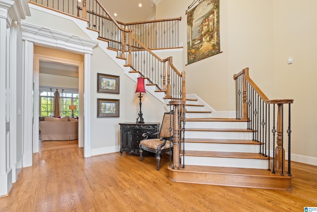 stairway with a wood stove, light hardwood / wood-style flooring, and a high ceiling