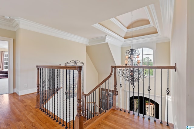 staircase with an inviting chandelier, crown molding, a tray ceiling, and wood-type flooring