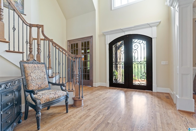 foyer entrance with decorative columns, french doors, hardwood / wood-style floors, and a towering ceiling