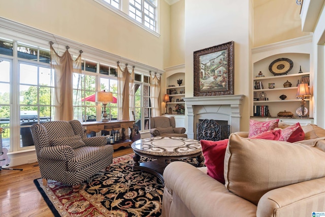 living room featuring wood-type flooring, built in shelves, and a towering ceiling