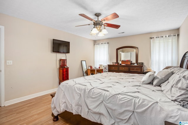 bedroom featuring baseboards, multiple windows, ceiling fan, and light wood-style floors
