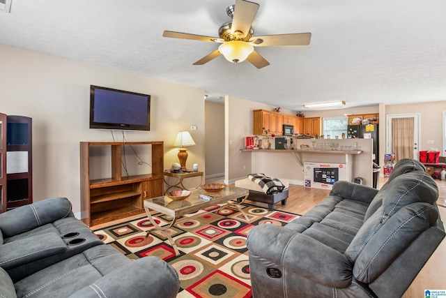 living room featuring baseboards, light wood-type flooring, ceiling fan, and a textured ceiling