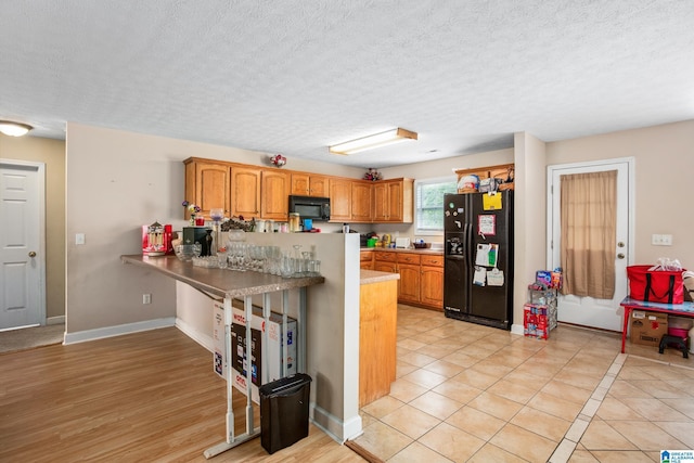 kitchen featuring a textured ceiling, light countertops, a peninsula, brown cabinets, and black appliances