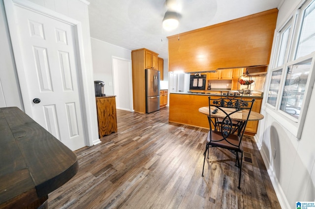 kitchen with dark wood-type flooring, stainless steel refrigerator, black gas cooktop, a kitchen bar, and kitchen peninsula