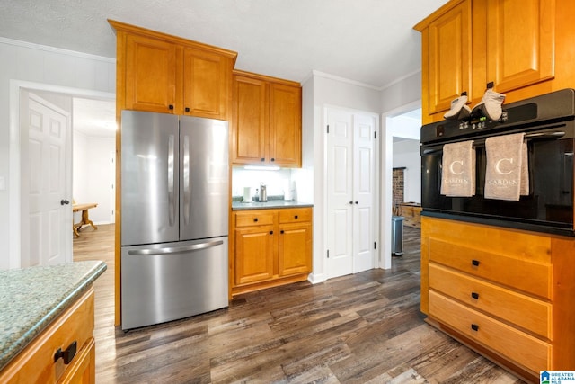 kitchen with ornamental molding, dark hardwood / wood-style floors, black oven, and stainless steel refrigerator