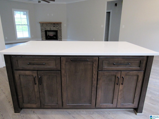 kitchen featuring light wood-type flooring, dark brown cabinets, a center island, a brick fireplace, and ceiling fan