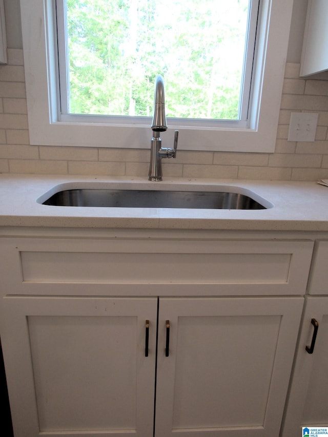 details with decorative backsplash, white cabinets, sink, and light stone countertops