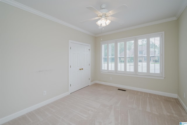 empty room featuring ceiling fan, light colored carpet, and ornamental molding