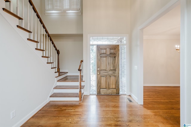 foyer featuring light hardwood / wood-style flooring, crown molding, and a towering ceiling