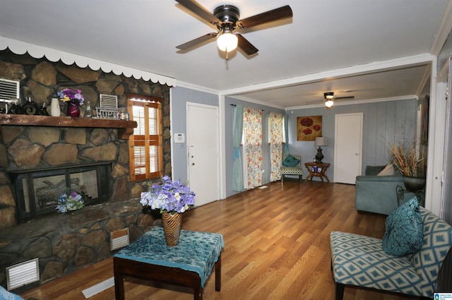 living room with ceiling fan, crown molding, a fireplace, and wood-type flooring