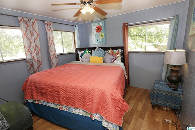 bedroom featuring ceiling fan, multiple windows, wood walls, and wood-type flooring