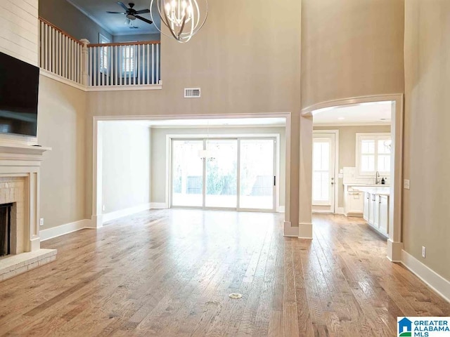 unfurnished living room featuring a towering ceiling, ornamental molding, a fireplace, and light hardwood / wood-style floors