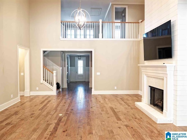 unfurnished living room featuring hardwood / wood-style flooring, a towering ceiling, a chandelier, and a fireplace