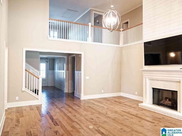 unfurnished living room with wood-type flooring, ornamental molding, a notable chandelier, a towering ceiling, and a fireplace