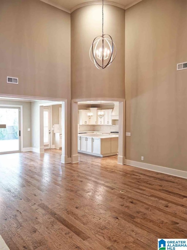 unfurnished living room featuring a notable chandelier, crown molding, wood-type flooring, and a high ceiling