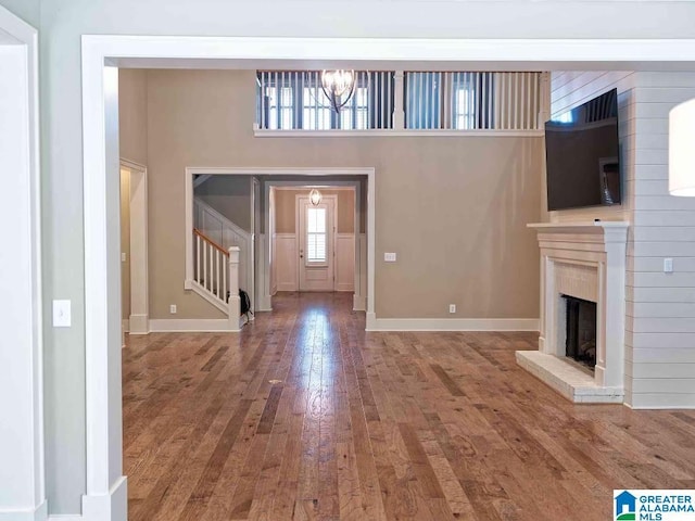 unfurnished living room featuring hardwood / wood-style flooring, a chandelier, and a brick fireplace