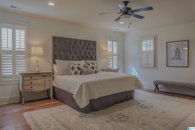 bedroom featuring ceiling fan, ornamental molding, wood-type flooring, and multiple windows