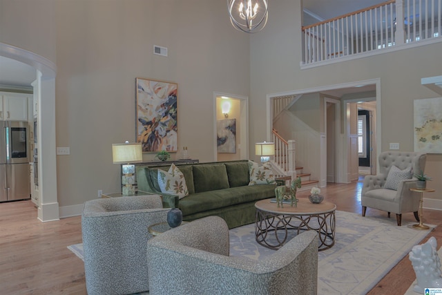 living room with a towering ceiling, an inviting chandelier, and light hardwood / wood-style flooring