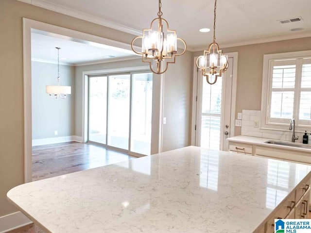 kitchen featuring sink, crown molding, decorative light fixtures, a chandelier, and light stone countertops