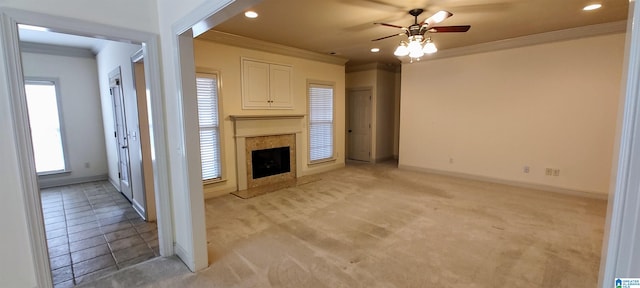 unfurnished living room featuring a high end fireplace, crown molding, light carpet, and ceiling fan