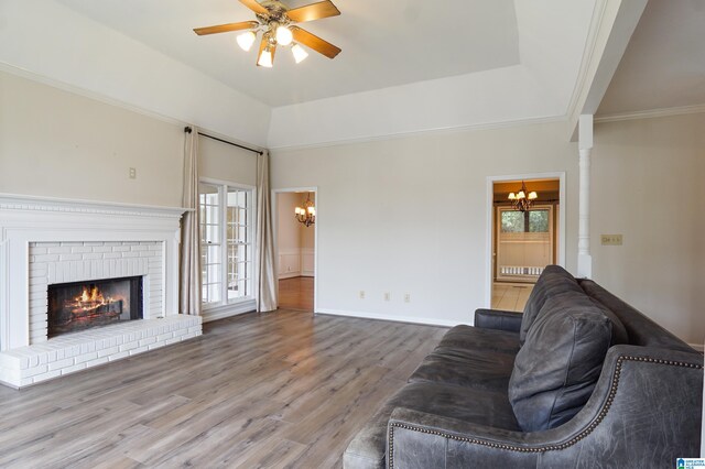 living room featuring wood-type flooring, a brick fireplace, ceiling fan with notable chandelier, a raised ceiling, and ornate columns