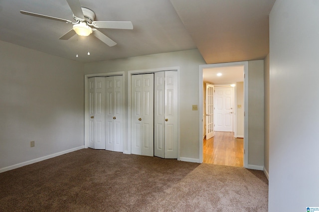 unfurnished bedroom with two closets, light colored carpet, and ceiling fan