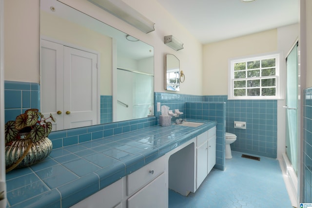 bathroom with a shower with door, tile walls, vanity, tile patterned floors, and toilet