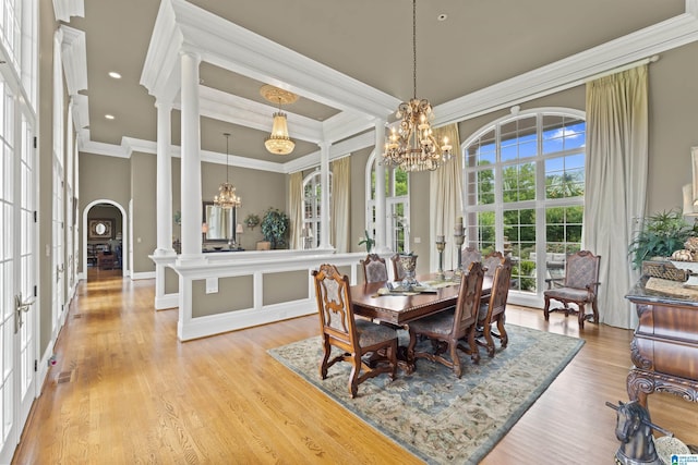 dining area with an inviting chandelier, crown molding, ornate columns, and light wood-type flooring